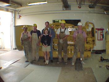 Caterpillar 3512 diesel engine generator rigged into the building and ready to be placed into the engine room directly behind the skid. Group shop with site workers.