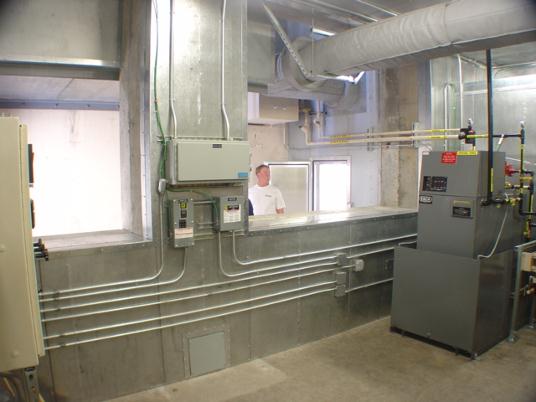 1100 kW standby emergency diesel generator installation showing air inlet, exhaust stack, control panel and load bank controls.